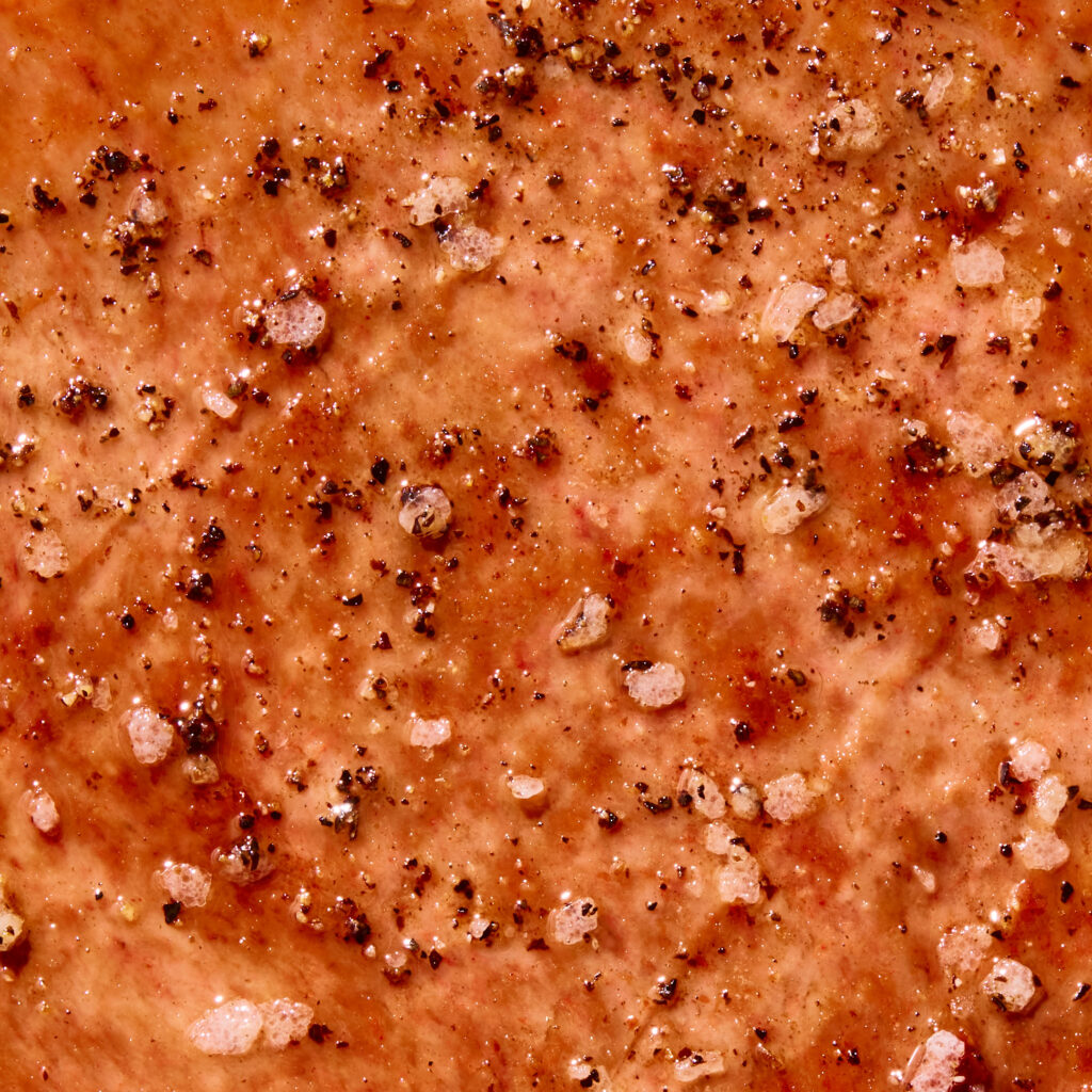 Close-up of seasoned meat with salt and pepper on a brown background